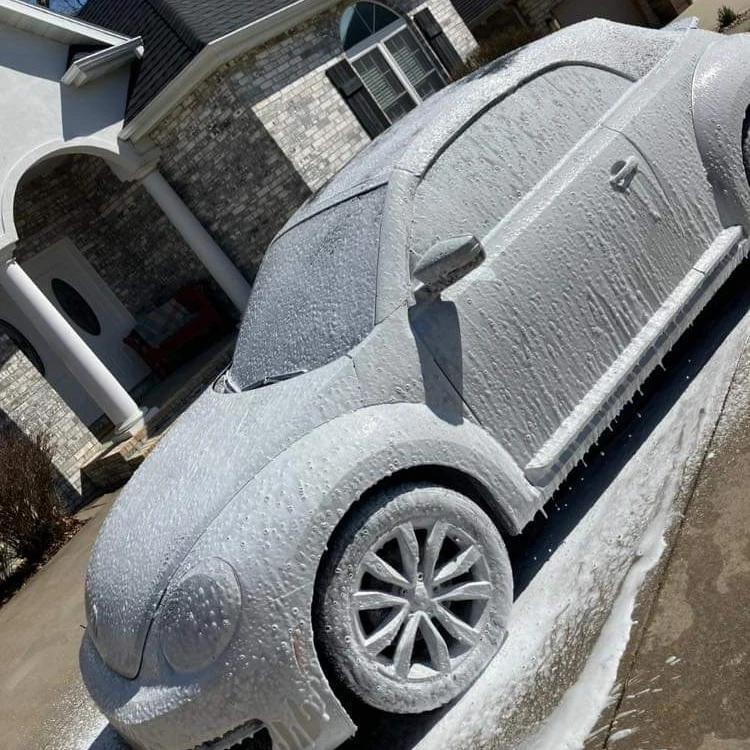 A car under a full coat of snow foam on a driveway